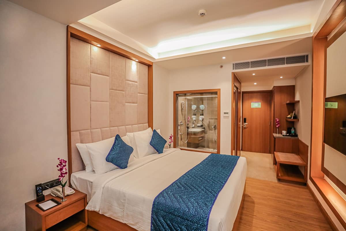 A hotel room with a bed, bedside table, nightstand, and a bathroom with a glass door.