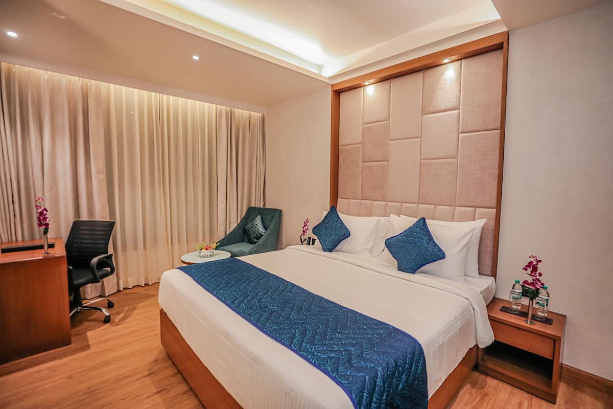 A hotel room with a large bed, a desk, a chair, and a nightstand with a vase of flowers.