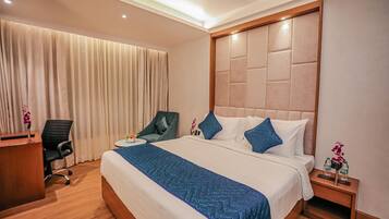 Een hotelkamer met een groot bed, een bureau, een stoel en een nachtkastje met een bloemenvaas.