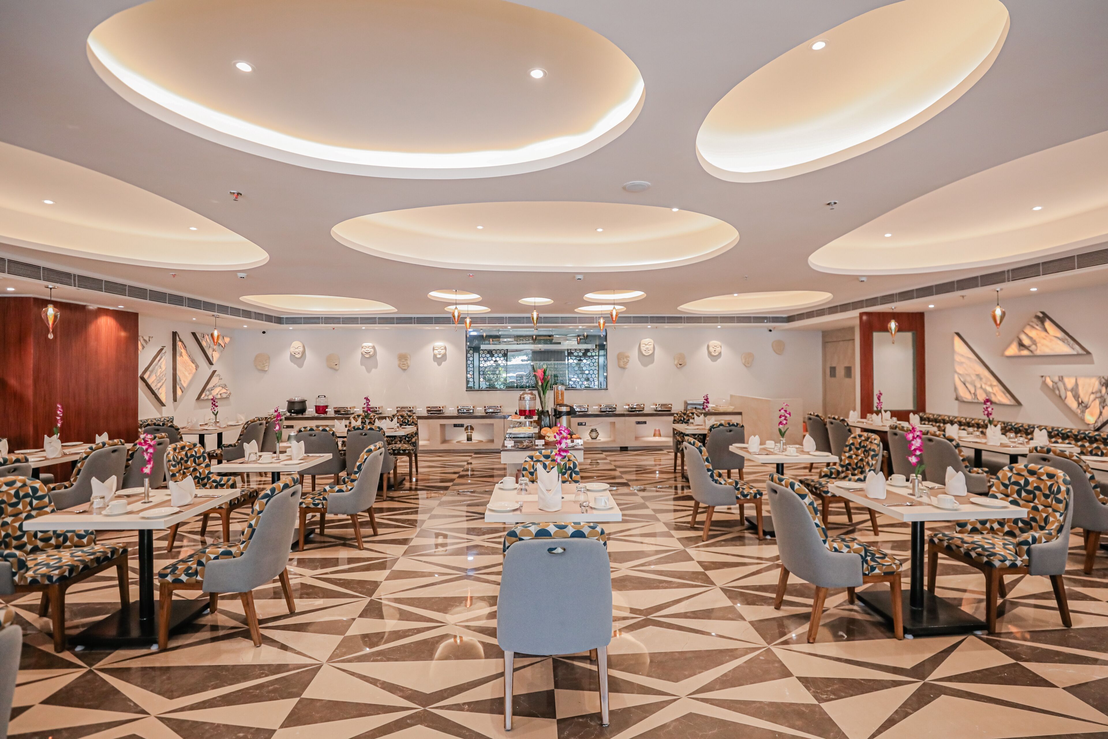 A spacious dining area with multiple tables and chairs, a patterned floor, and a central island with a view of the outdoors.