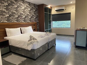 Ein modernes Hotelzimmer mit einer Ziegelwand, einem großen Bett mit weißer Bettwäsche, einem Holz-Kopfteil, einem kleinen Schreibtisch und einem Fenster mit Blick auf Grünflächen.