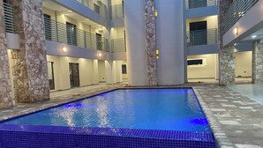 Ein Pool mit blau gefliesten Rändern, umgeben von steinernen Säulen und einem mehrstöckigen Gebäude mit Balkonen.