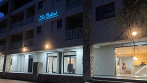 Ein Hotel mit dem Schild "The Outlook Victoria Falls". Es hat eine Steinfassade, mehrere Balkone und einen gut beleuchteten Eingang mit Stufen zum Eingang.