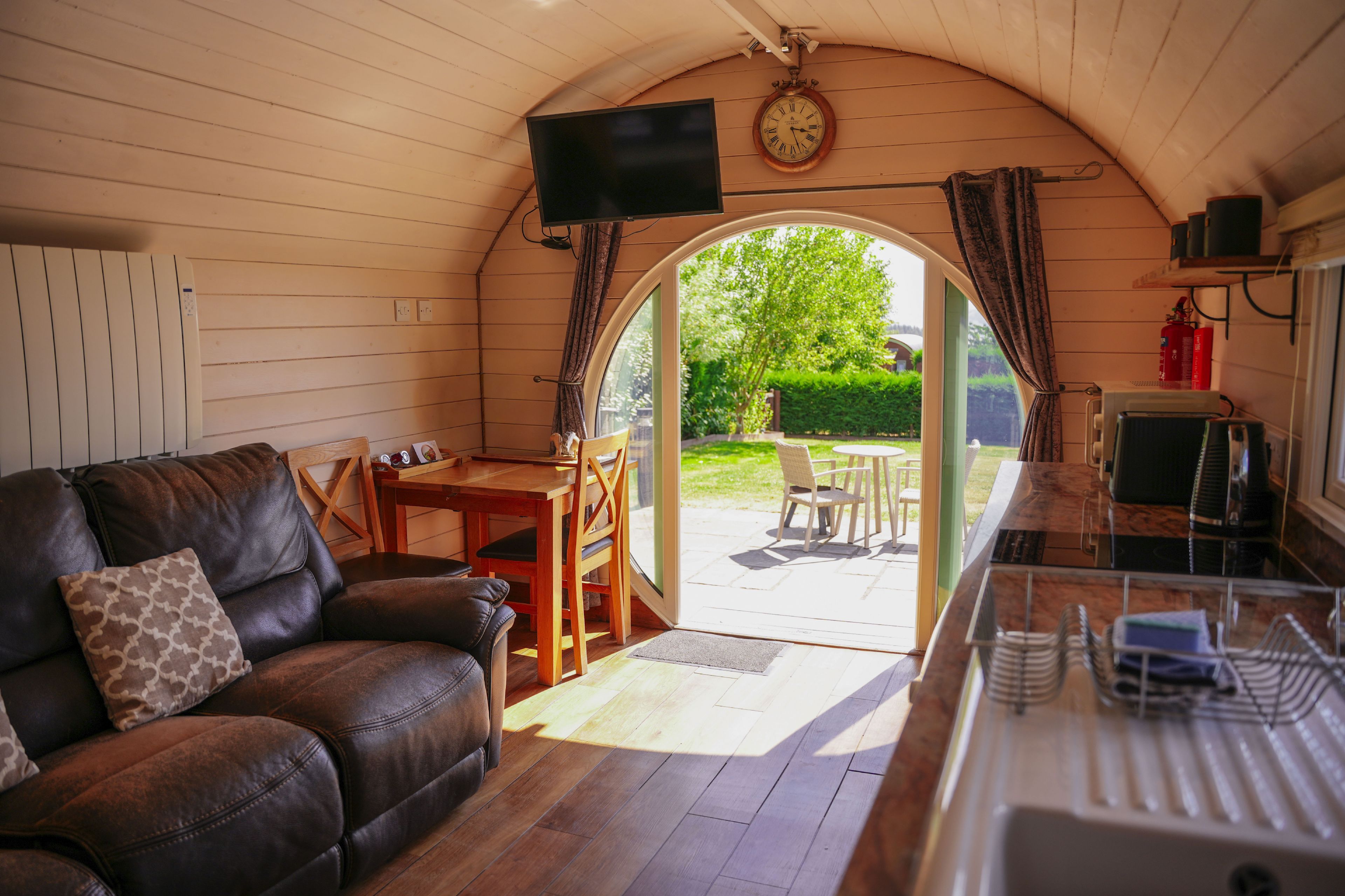 Ein gemütliches Interieur mit Ledersofa, Fernseher und Essbereich, der zu einem Garten führt.