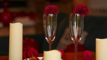 A table with candles, a bowl of flowers, and two champagne flutes with red flowers.