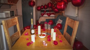Een gezellige eethoek met een houten tafel gedekt voor twee, omringd door rode ballonnen en bloemen.