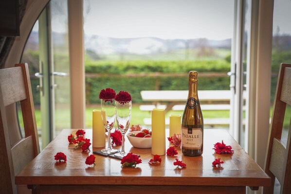 A table with a bottle of wine, candles, and red flowers. - Meadow View - Glamping pod sleeping 2 guests, Pet Friendly (Rhayader)