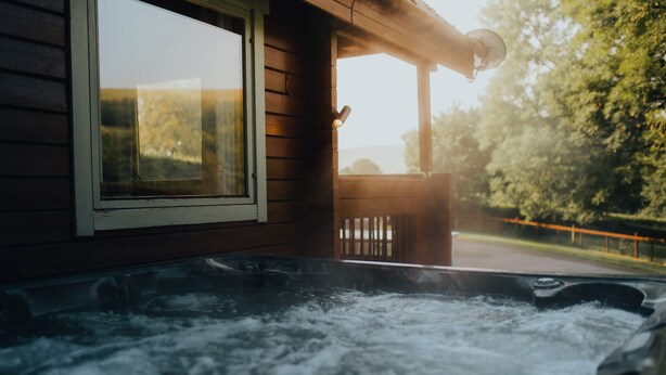 Un bain à remous avec un rev êtement extérieur en bois, offrant une vue sur les arbres et une clôture.