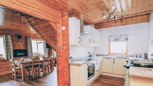 Une cuisine chaleureuse avec des poutres en bois, des armoires blanches et un coin repas comprenant une table et des chaises.