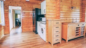 L’intérieur d’une cabane en bois comprend un coin cuisine équipé d’un lave-linge, d’un four à micro-ondes et de meubles de rangement en bois.