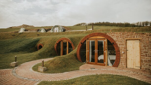 A building with circular windows and a brick exterior. - Otters View -  Underground Hobbit Home Sleeping 6 guests, Pet Friendly (Rhayader)