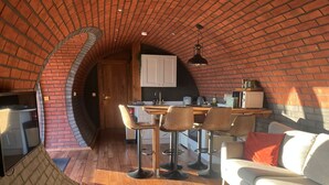 A cozy kitchen with a brick archway leading to a dining area, featuring a wooden table and bar stools. - Otters View -  Underground Hobbit Home Sleeping 6 guests, Pet Friendly (Rhayader)