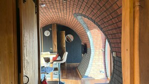 A narrow hallway with a brick ceiling and wooden walls, leading to a seating area with a fire extinguisher and a clock on the wall. - Otters View -  Underground Hobbit Home Sleeping 6 guests, Pet Friendly (Rhayader)