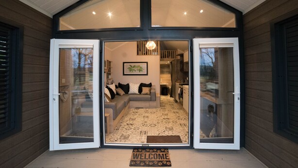 Ein modernes Haus mit einladendem Eingang, einem Wohnzimmer mit Sofa und Teppich, und einer durch die offene Tür sichtbaren Küche.