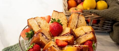 Een bord met plakjes brood en aardbeien, een rieten mand vol fruit en een groene linnen servet.