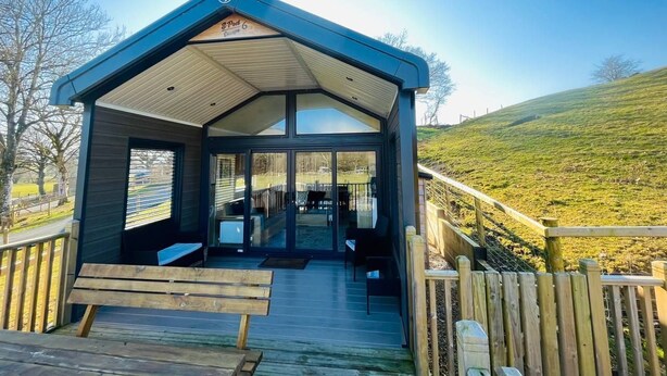 A covered outdoor area with a wooden deck, benches, and a glass door leading to an interior space.