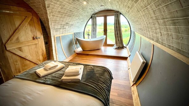 Une chambre à coucher avec un grand lit, une porte en bois et une vue sur un paysage verdoyant, visible à travers une fenêtre circulaire.