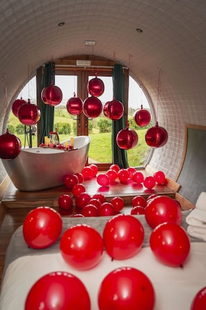 A bedroom with a large window, a bathtub, and red balloons.