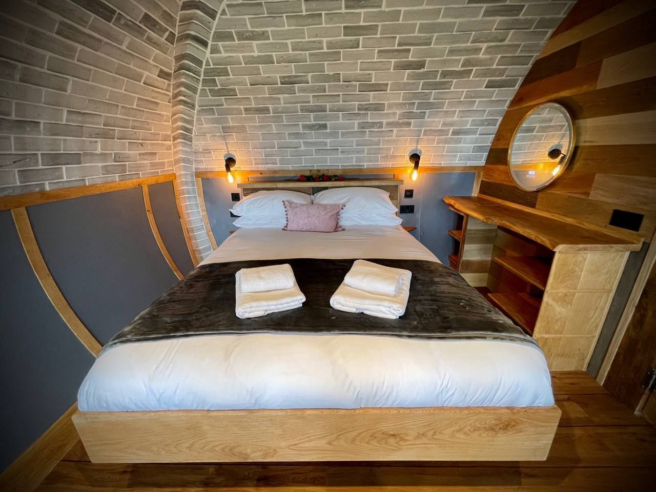 Un lit avec une tête de lit, deux tables de chevet, un miroir et un banc en bois.