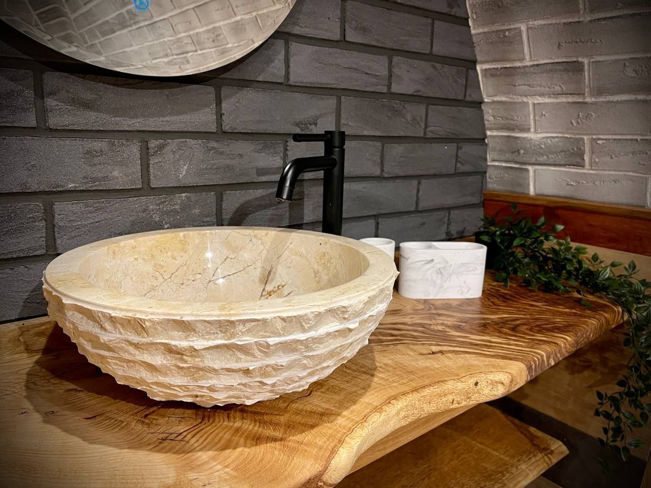 A stone sink with a wooden countertop, a black faucet, and a white cup beside it.