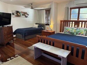 A bedroom with a bed, a desk, a chair, a dresser, a television, and a window with blinds.