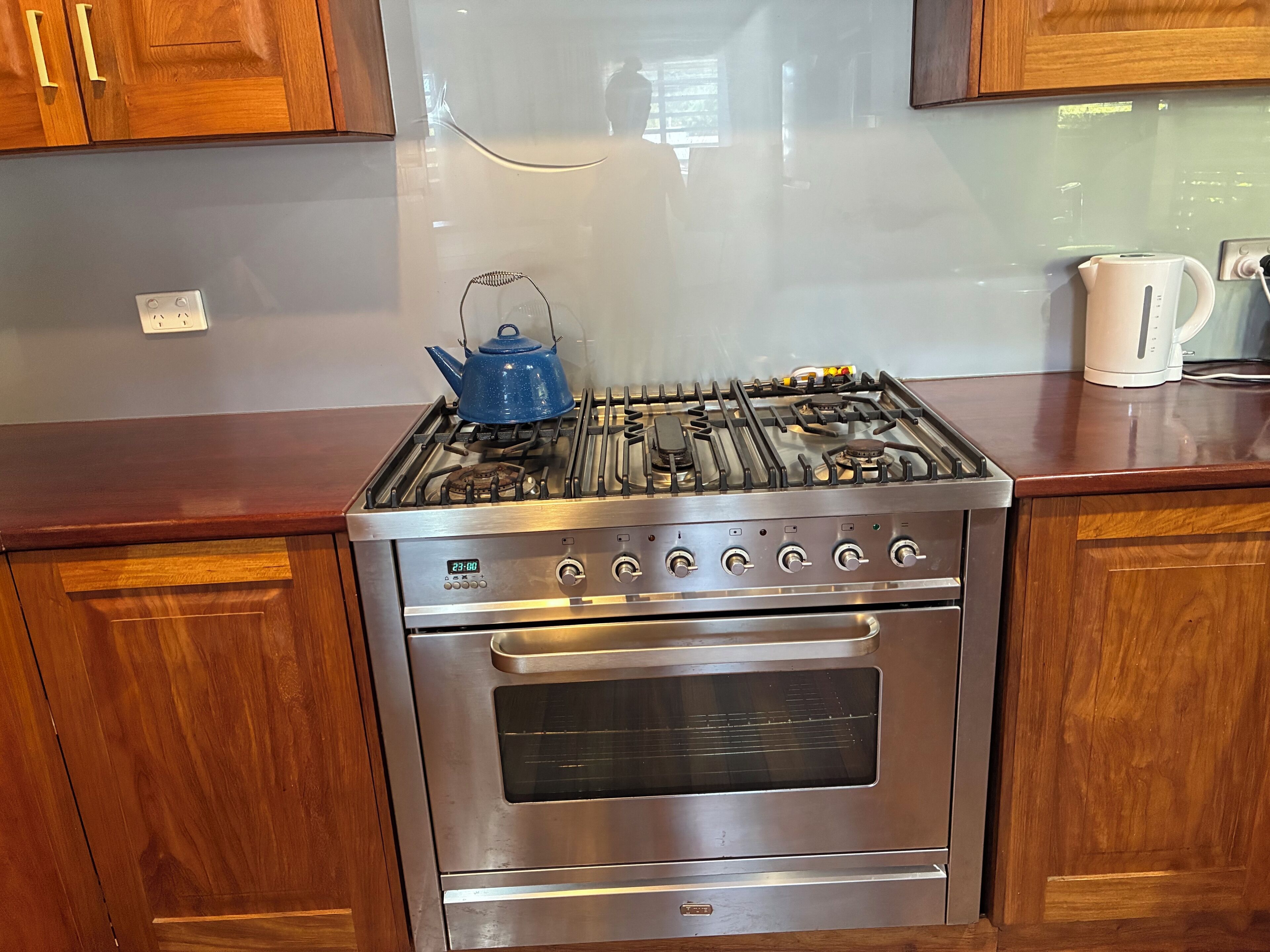 A stainless steel kitchen with a gas stove, oven, and a blue kettle on the countertop.