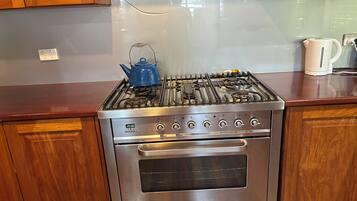 A stainless steel kitchen with a gas stove, oven, and a blue kettle on the countertop.