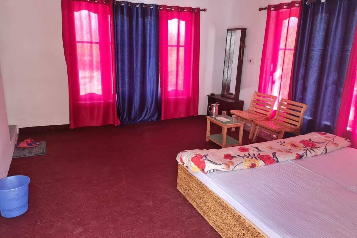A room with a bed, a wooden chair, a small table, and a red carpet.