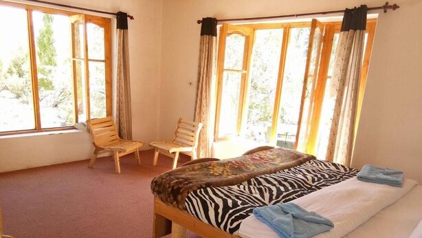A room with a single bed, two chairs, and large windows.