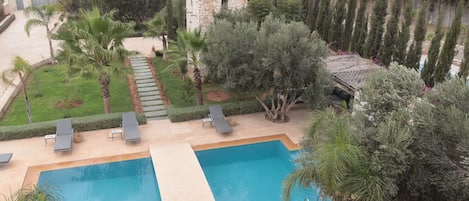 Zona de piscina con dos piscinas, sillones de descanso y una torre de piedra.
