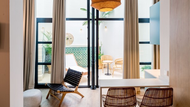 A modern room with large windows, a hanging light fixture, and wicker furniture. - Honest Sevilla (Seville)