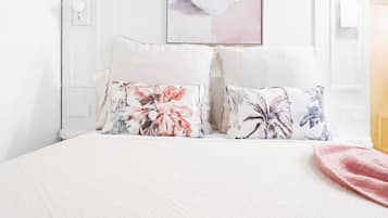 A neatly made bed with floral pillows, a pink blanket, and a framed artwork above the bed.