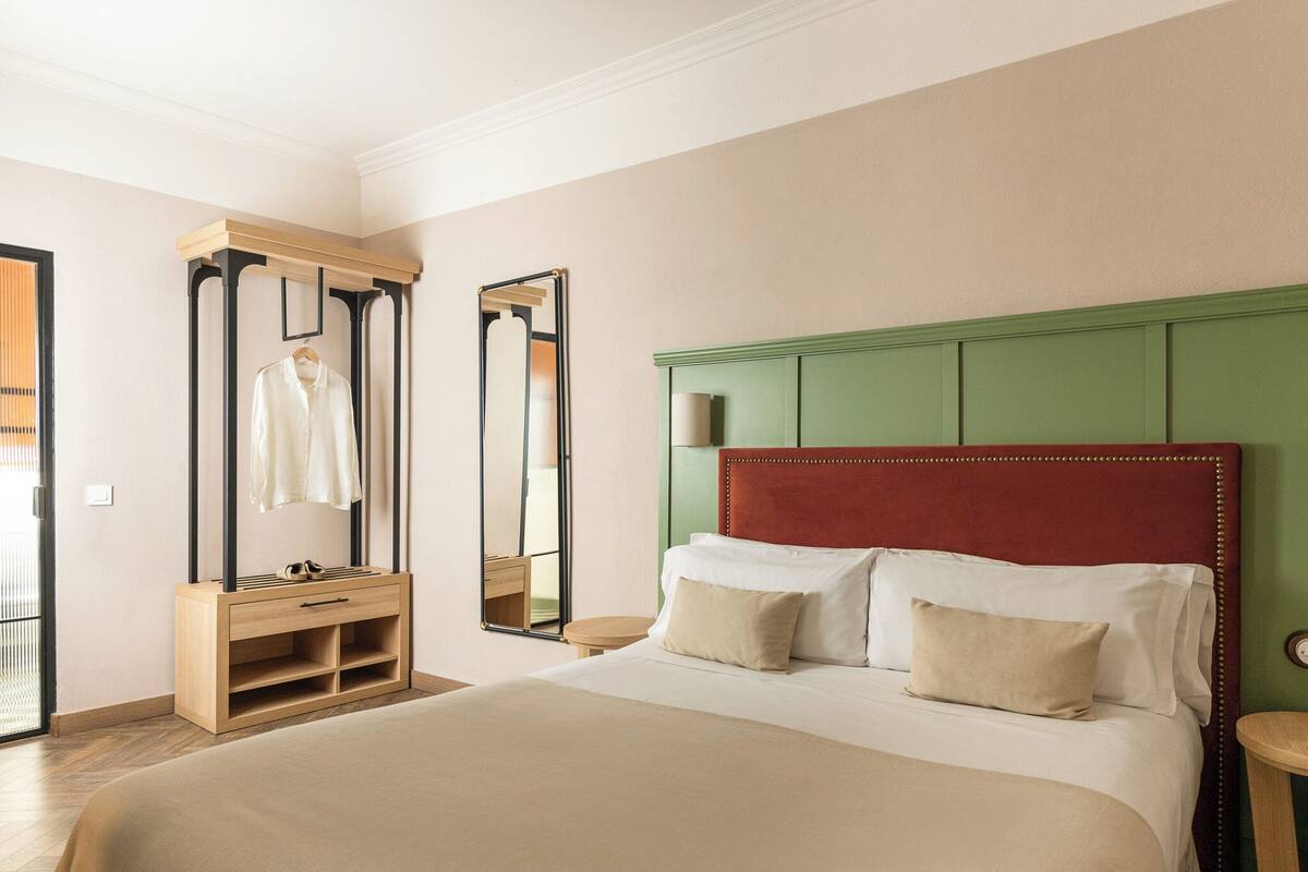 A hotel room with a bed, a wooden dresser, a mirror, and a green headboard.