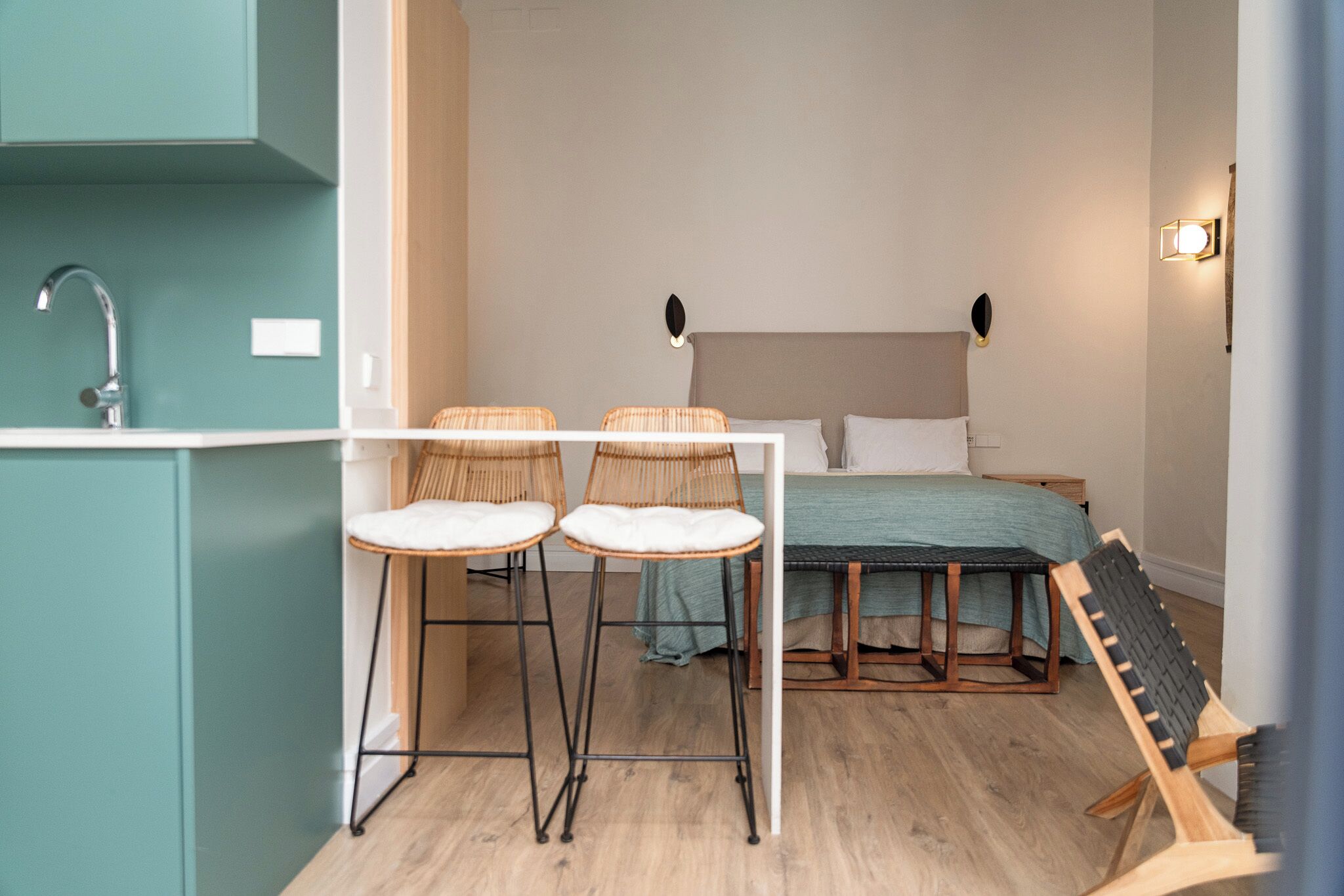 A compact bedroom with a bed, two chairs, a small table, and a wooden chair.