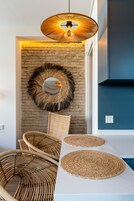 Una cocina moderna con pared de ladrillo, lámpara colgante, sillas de mimbre y individuales tejidos.