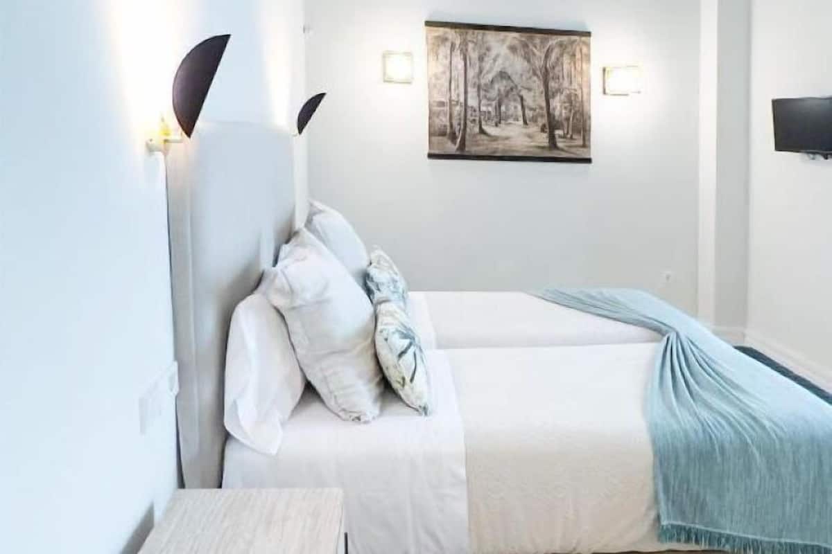 A bedroom with a bed, bedside table, and a painting on the wall.