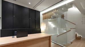 A modern reception desk with a wooden finish, a black wardrobe, and a glass wall with a staircase. - Casa Bella Gracia by Aspasios (Barcelona)
