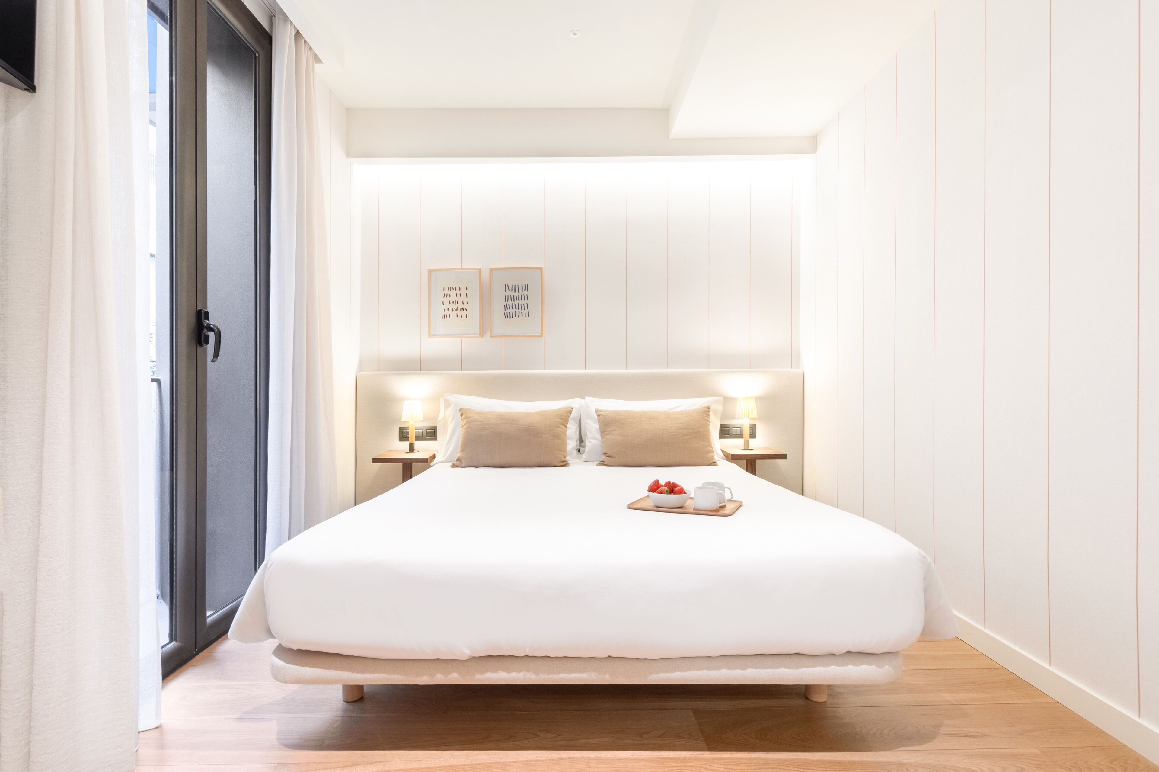 Un dormitorio moderno con una cama grande, mesitas de noche con lámparas y vistas al exterior a través de una puerta corrediza.