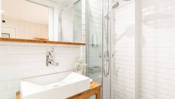 A modern bathroom with a white sink, wooden vanity, and a glass shower enclosure.