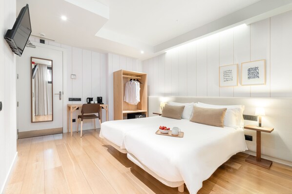 Habitación de hotel moderna con una cama grande, mesita de noche con lámpara, armario de madera, escritorio con silla y televisor de pantalla plana montado en la pared.