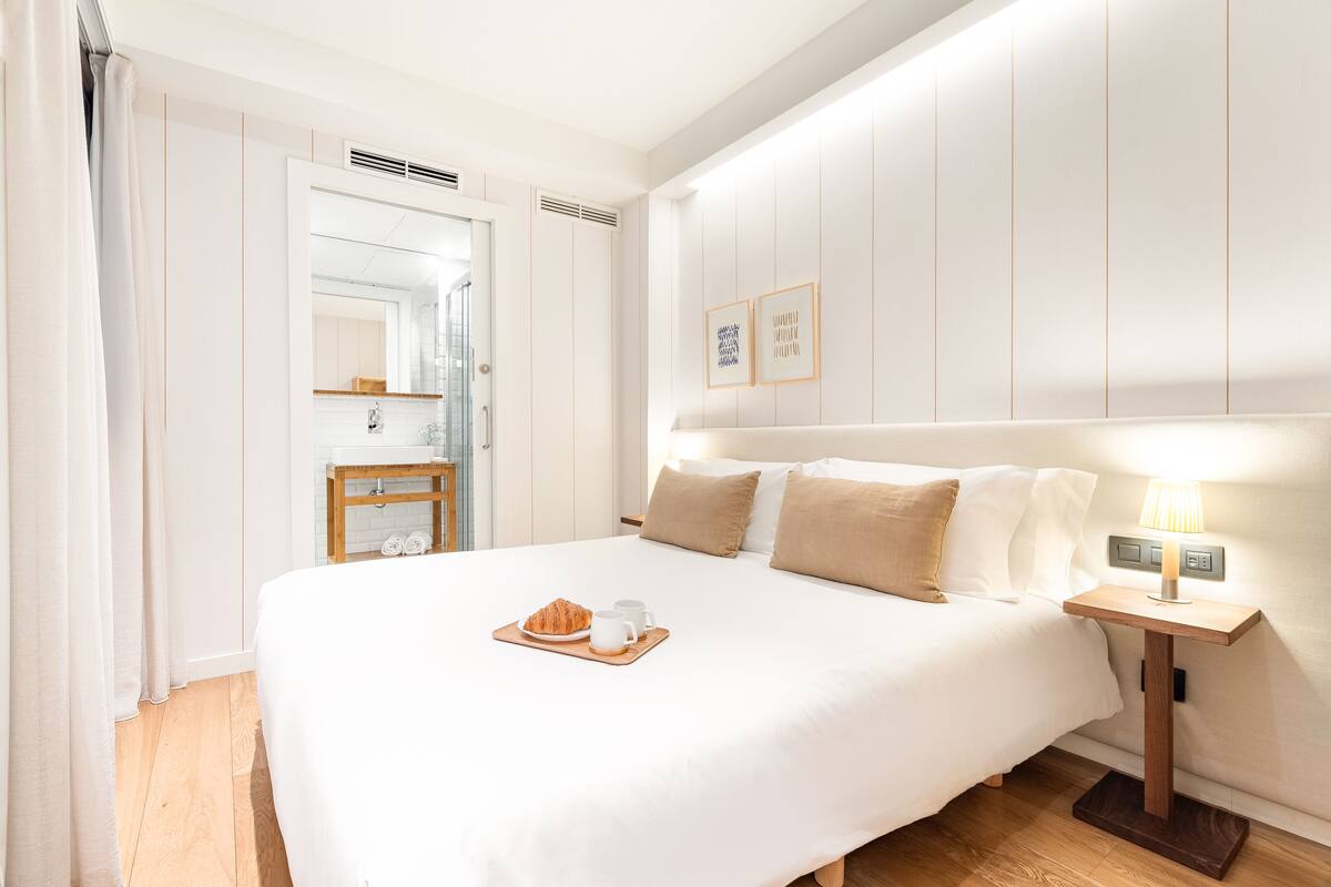 Een hotelkamer met een groot bed, een nachtkastje met een lamp en een ontbijttray op het bed.