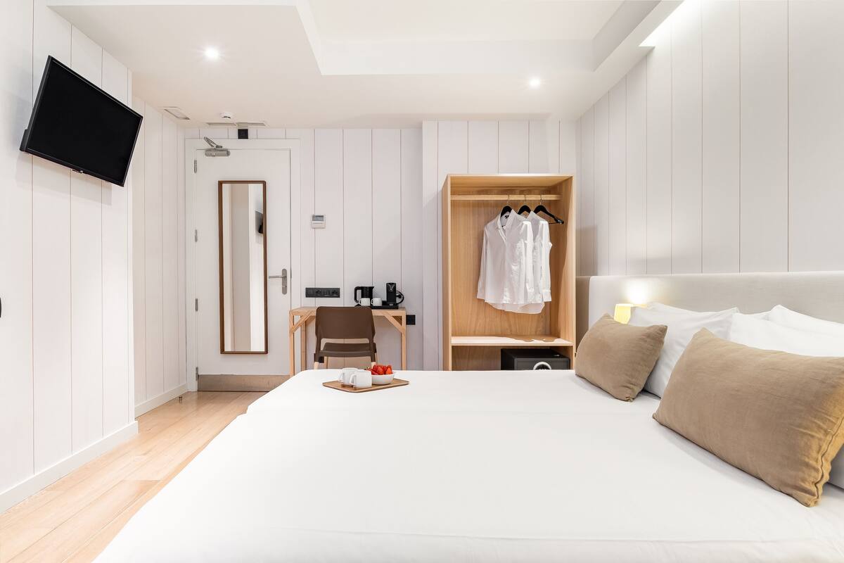 Een moderne hotelkamer met een groot bed, een kledingkast, een bureau met stoel, een televisie en een spiegel.