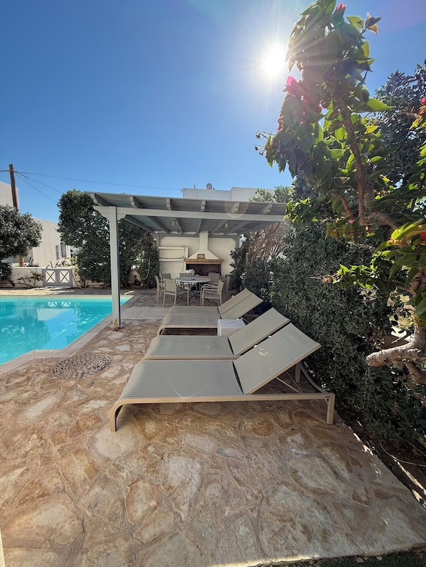 Un espace aménagé au bord de la piscine, comprenant des chaises longues, une pergola et un barbecue.