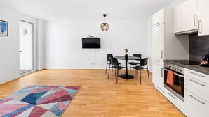 Une cuisine moderne avec des meubles blancs, un four encastré et un coin repas comprenant une table ronde et des chaises.