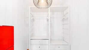 Une armoire blanche avec deux tiroirs et une tringle à vêtements, située dans une pièce dont le sol est en bois et les murs sont blancs.
