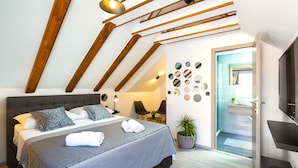 A modern bedroom with a large bed, wooden beams, a TV, and a bathroom visible through an open door. - Sirius Luxury Rooms (Split)