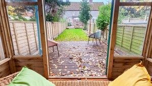 A room with a view of a backyard through large windows. - Sunny Beck Cottage - cosy cottage in Mundesley (Mundesley)