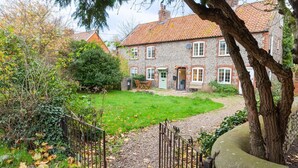 A stone house with a tiled roof, a grassy yard, and a metal fence. - Sunny Beck Cottage - cosy cottage in Mundesley (Mundesley)