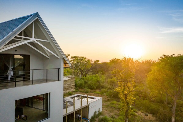 Un bâtiment moderne à deux étages, doté de grandes fenêtres et d’un balcon, entouré d’une végétation luxuriante et surplombant un ciel dégagé.