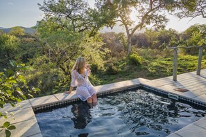 A woman sitting by a pool surrounded by lush greenery and trees. - Kruger Cliffs Lodge (Hoedspruit)